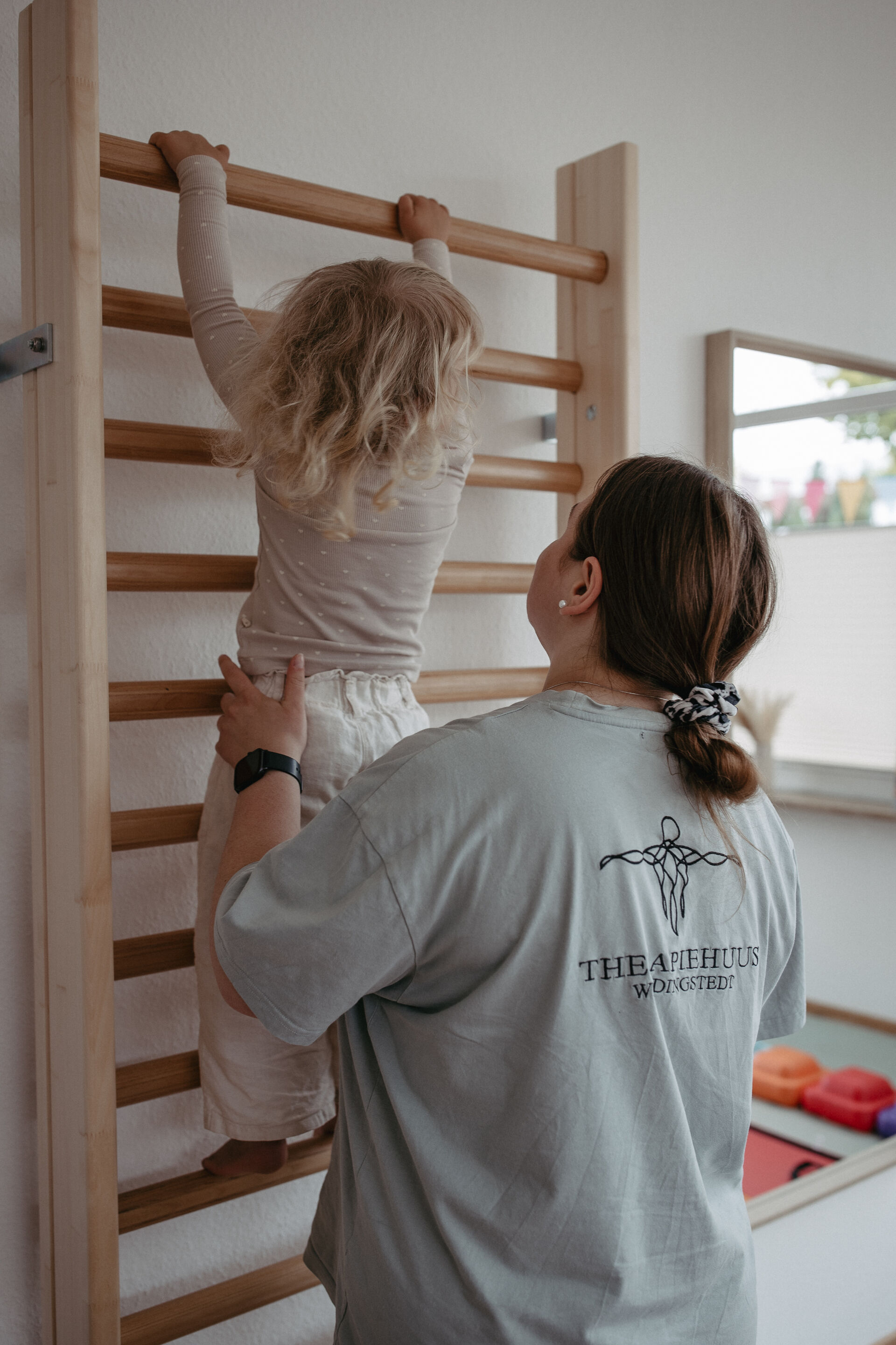 Praxis Interior - Therapeutin hilft Kind an der Sprossenwand